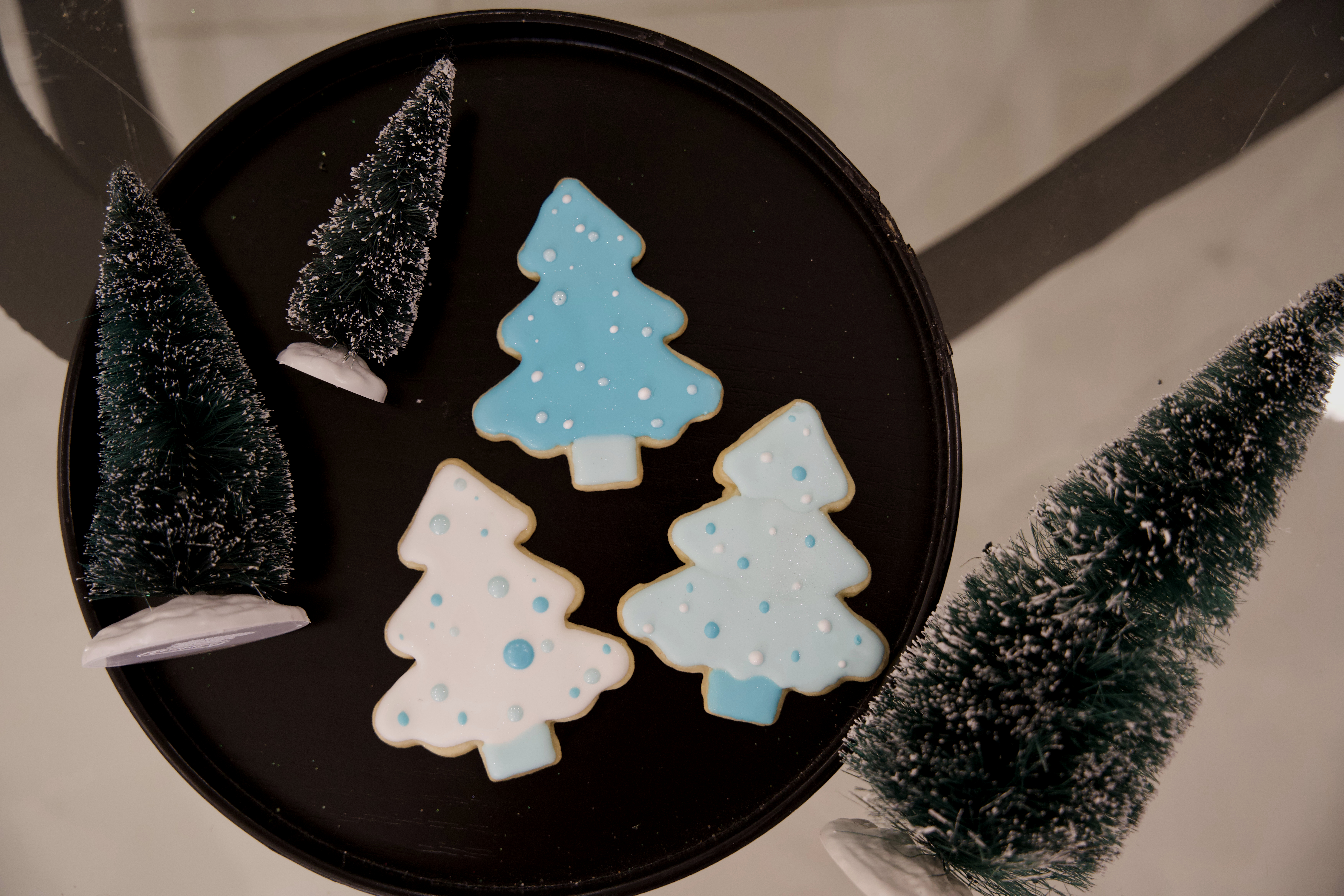 three sugar cookies decorated on a plate with other fake tree decor around them. 