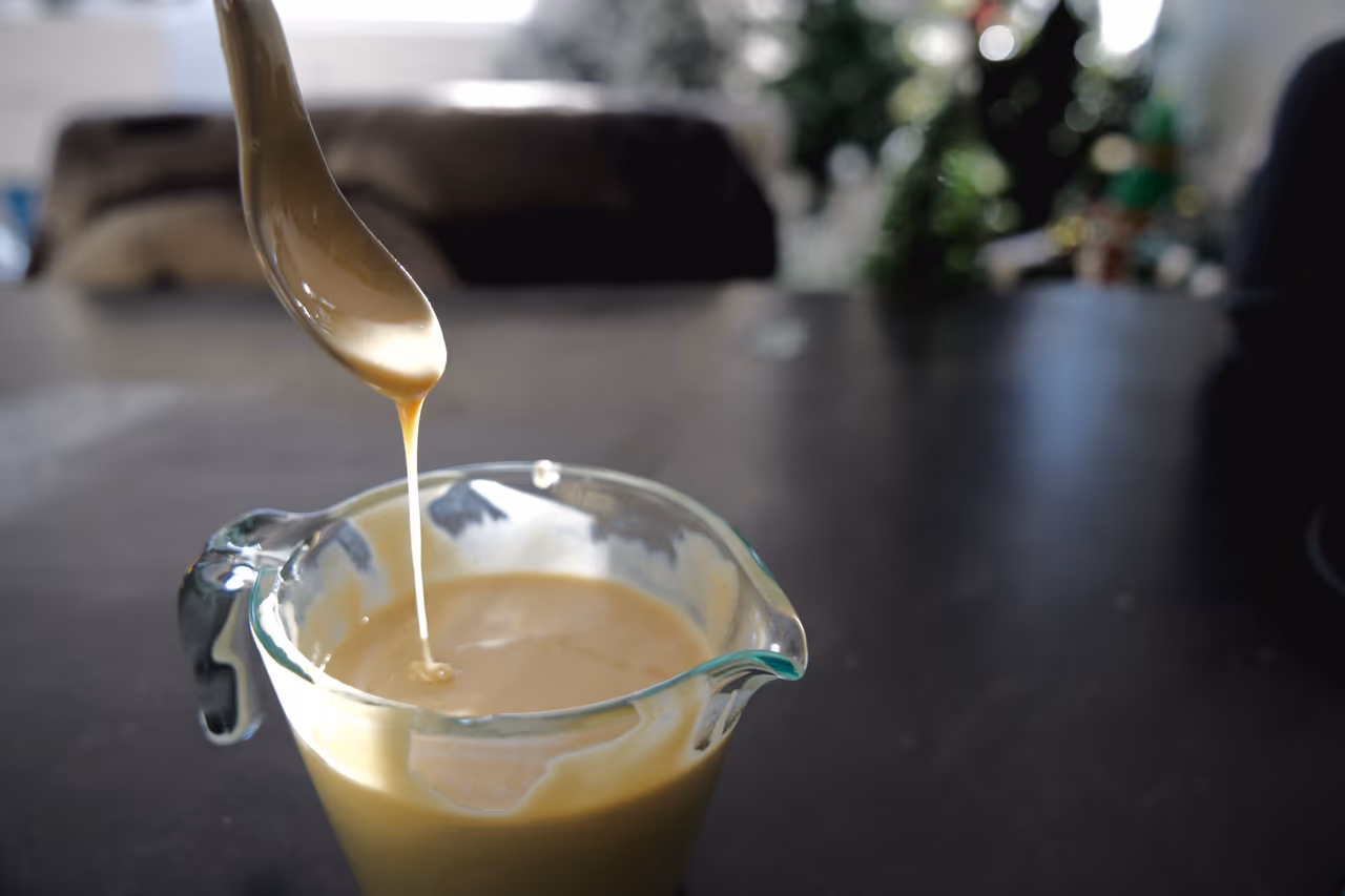 brown sauce dropping off a spoon into a measuring cup.