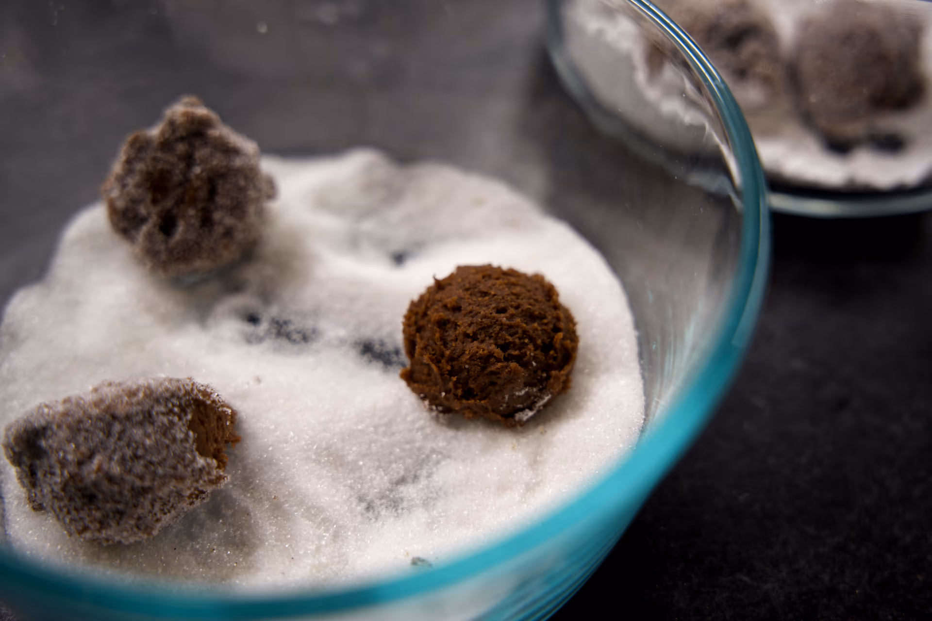 chocolate cookies being rolled in granulated sugar.