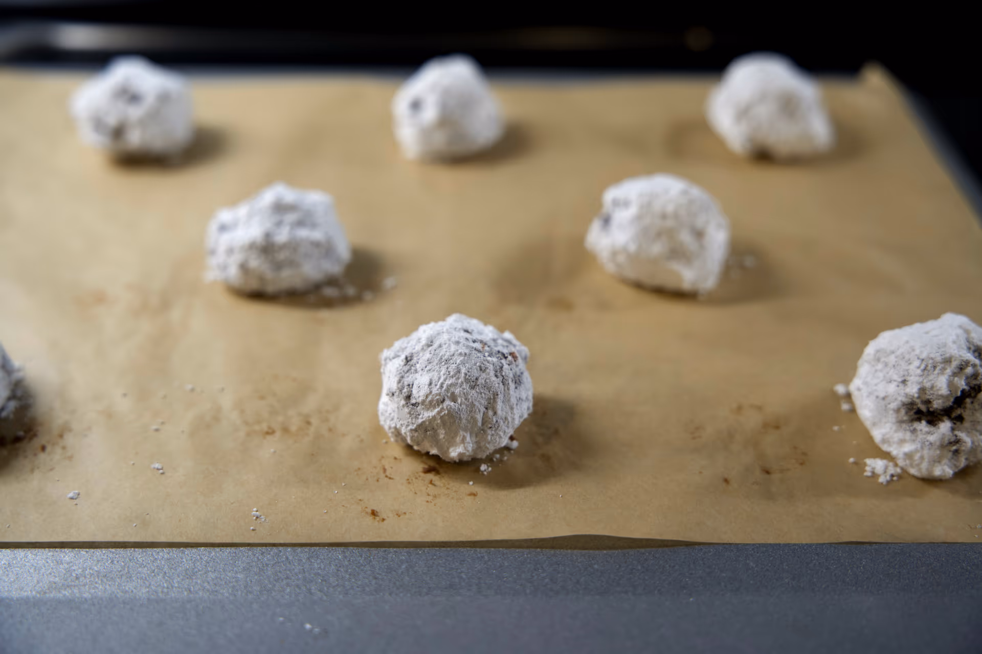 chocolate cookies rolled in powdered sugar on parchment paper.
