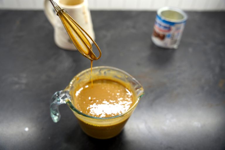 Gingerbread sauce dripping off a whisk into a glass measuring cup. 