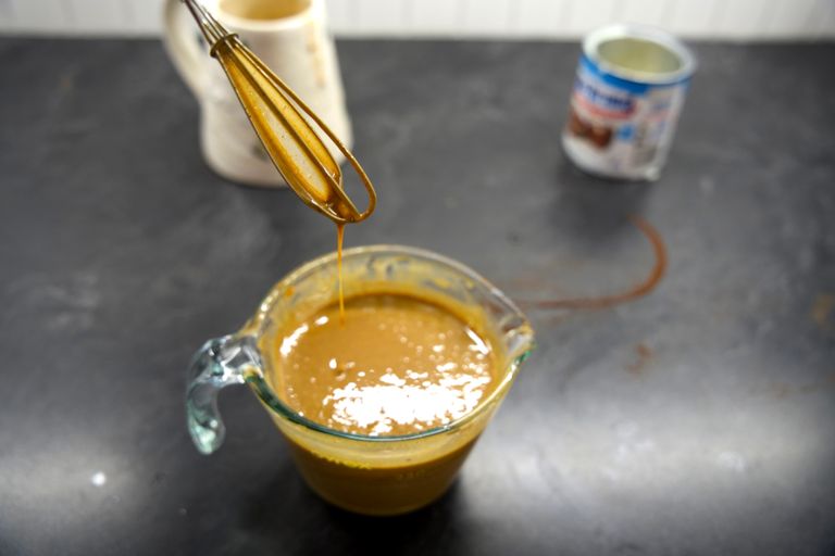 Gingerbread sauce dripping off a whisk into a glass measuring cup.
