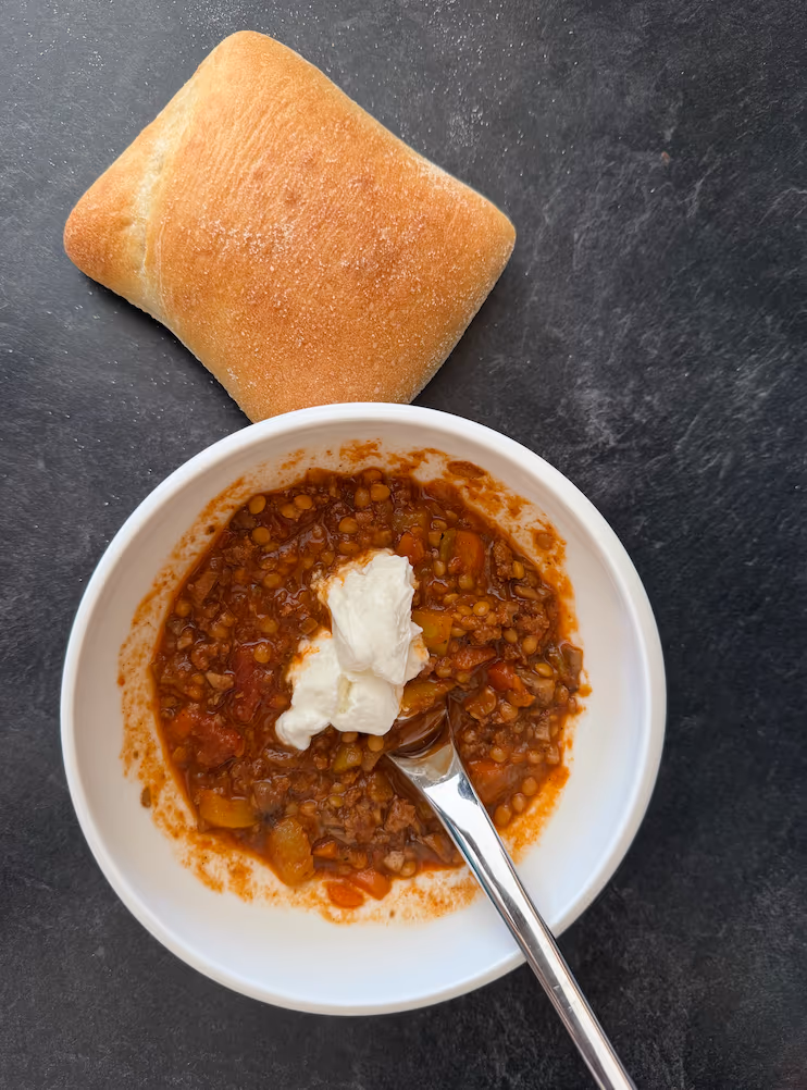 Bowl of chili with yogurt and bun.
